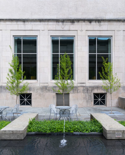 Courtyard at the Cincinnati Art Museum, featuring a table and chairs, flanked by a row of trees behind it and small fountains that separate the table spaces in front.
