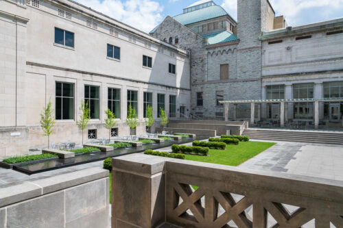 Courtyard at the Cincinnati Art Museum, featuring a row tables and chairs, flanked by a row of trees on the left and small fountains that separate the table spaces on the right.