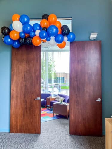 A balloon arch with orange, blue, black, and white balloons hangs over The Lantz conference room at SMBH's office.