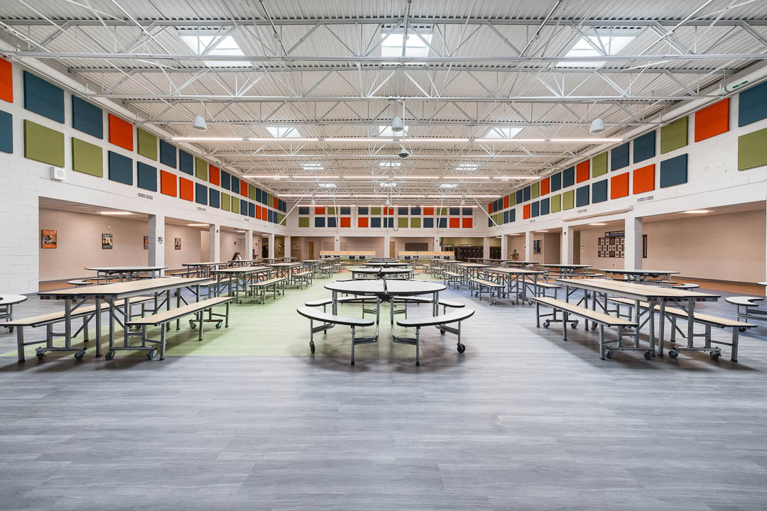 Interior photo of the common/dining area at McCord Middle School in Worthington, Ohio. Large space with vaulted ceilings filled with long rectangular and round tables to dining and activities.