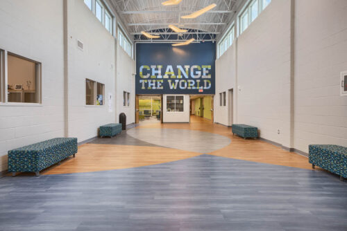 Interior entryway at Perry-Phoenix Middle School in Worthington, Ohio. A long hall with vaulted ceilings, concrete walls with small windows that runs the top of the wall. The end of the hall has "Change The World" painted on it.
