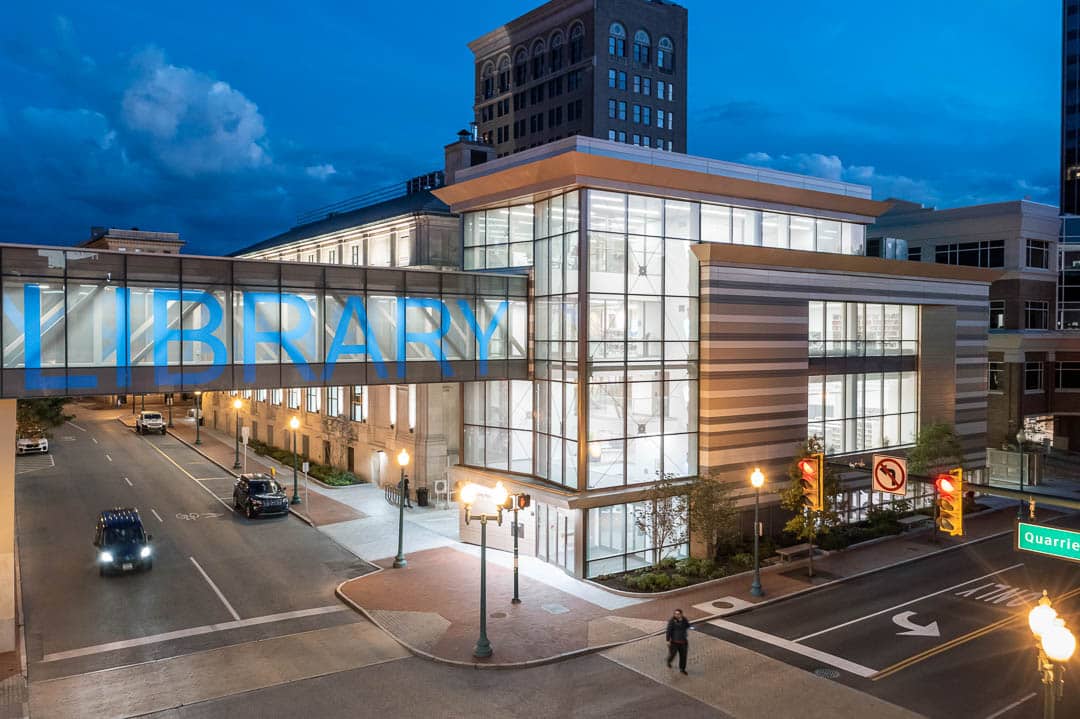 An exterior image of the Kanawha Public Library in Charleston, West VIrginia. Features the side of the building addition with a pedestrian bridge with the word "Library" written on it.