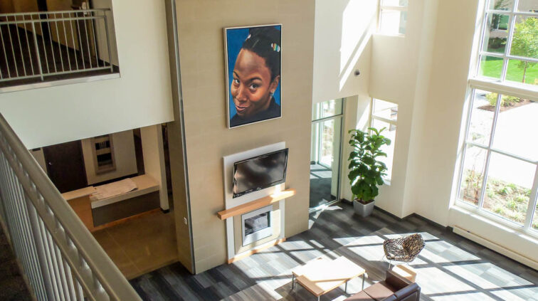 An interior view a common area at Falcon Heights and Centennial Hall at Bowling Green State University. Photo looks down on the common area from the level above. Common area features seating a fireplace next to large windows, which let in a lot of natural light.