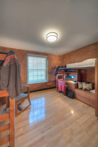Interior view of Lynn Hall dormitory rooms at Hanover College. Photo features a large brick room with two sets of bunkbeds and desks.