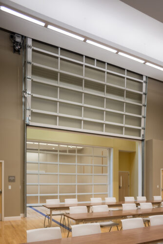 Interior photo of a classroom in Lynn Hall at Hanover College. Features long desks with chairs in front of a back wall that opens like a glass garage door.