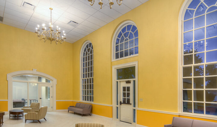 Photo of a common area in Lynn Hall at Hanover College. Features a vaulted ceilings and bright yellow walls with large, arched windows, with comfortable seating for small groups.
