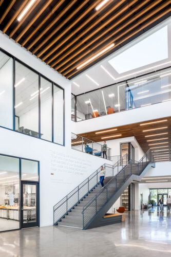Interior view of the main walkway and staircase in Mitchell Hall at Columbus Community College. Features high ceilings, large windows, and skylights that flood the bright, white area with natural light.
