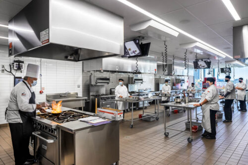 Interior photo of a test kitchen in Mitchell Hall at Columbus Community College. Looks like a commercial kitchen, with equipment and lots of stainless steel counter space to work on.