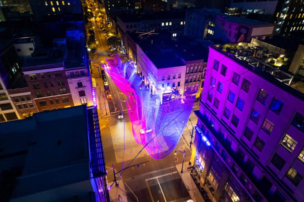 An aerial photo of Janet Echelman's "Current," hanging in downtown Columbus. Composed of different colors of twine and suspended from four different buildings.