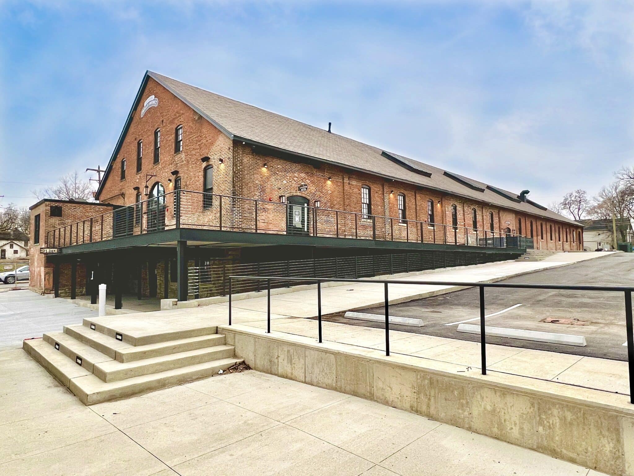 Exterior photo of the Historic Trolley Barn in Columbus, Ohio, which has been renovated and made into the East Market. A two-story brick building with a metal patio on both floors.