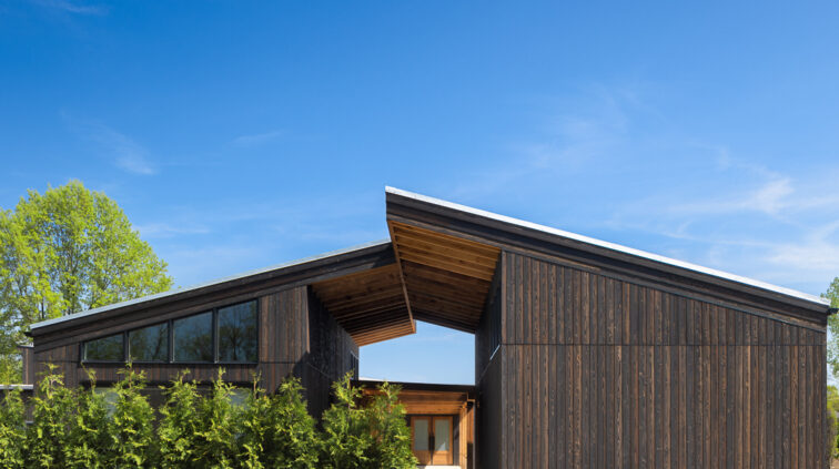 Exterior photo of The Gardens at Jorgensen Farms at dusk. The wood and glass structure is lit and glowing from within, against a blue sky in the background.